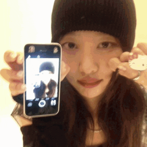 a woman wearing a black beanie is holding a cell phone