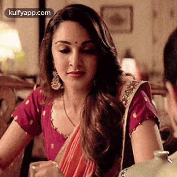 a woman in a saree is sitting at a table with a man and drinking tea .