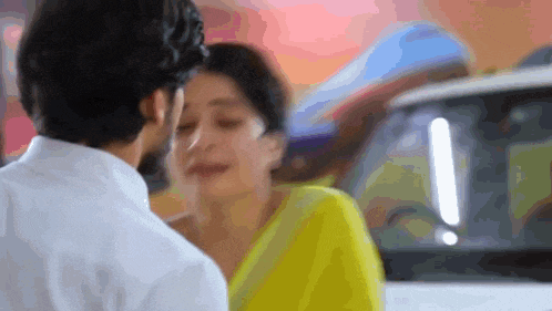 a man and a woman are kissing in front of a white car .