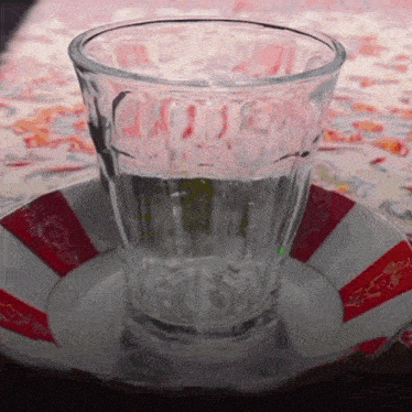 a glass of water sits on a red and white striped saucer
