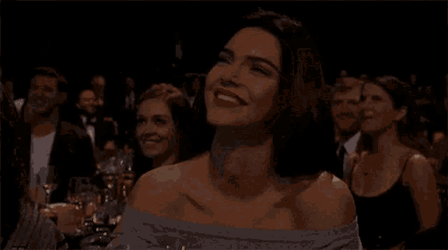 a woman is smiling while sitting in a crowd at a dinner party .