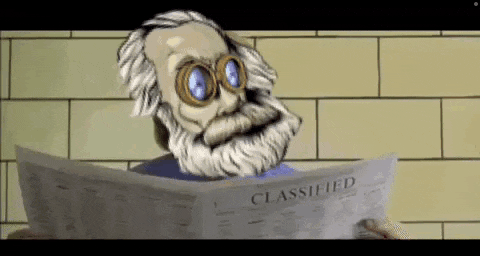 an elderly man with a beard and goggles is reading a classified newspaper .