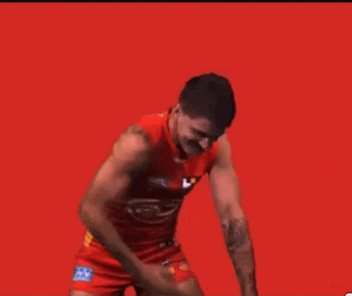 a man with a mustache is wearing a red tank top and shorts and is dancing on a red background .