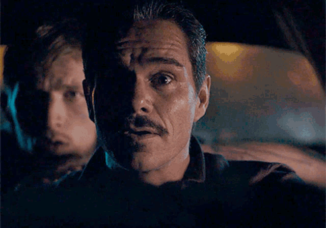 a man with a mustache is smiling while driving a car