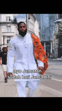 a man with a beard is walking down a street with the words ayo jumatan sudah hari jumat ini
