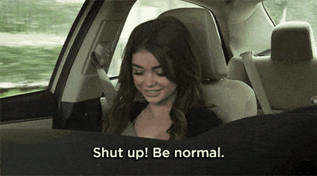 a woman is sitting in the back seat of a car and says " shut up ! be normal . "