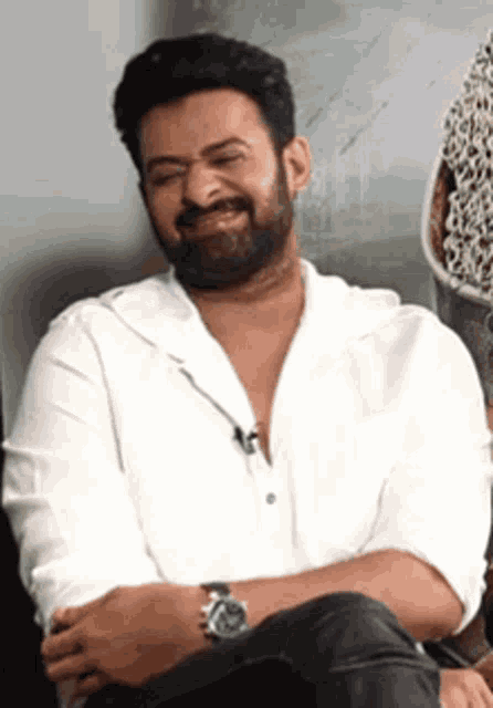 a man with a beard is wearing a white shirt and a watch while sitting down .