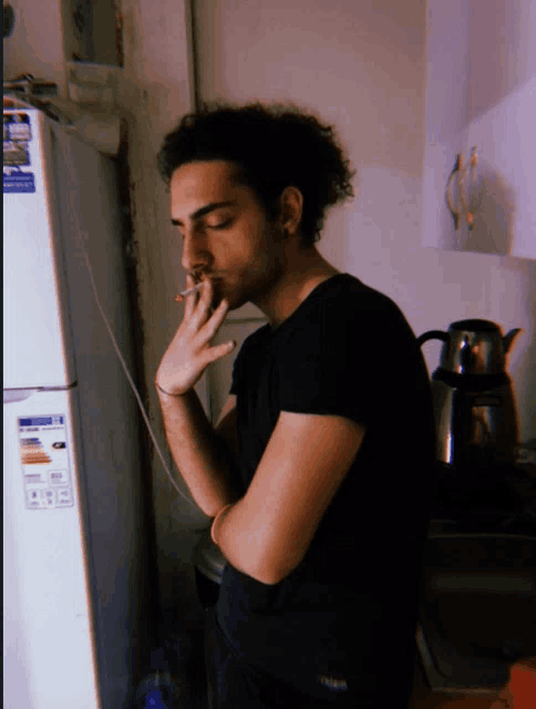 a man smoking a cigarette in front of a refrigerator that says ' samsung ' on it