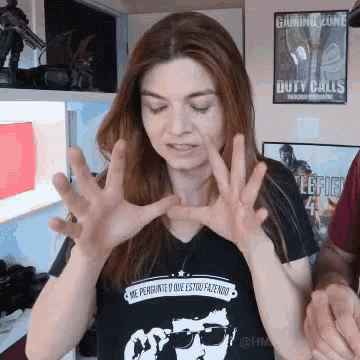 a woman wearing a black shirt that says me pergunte o que estou fazendo is making a gesture with her hands .
