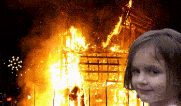 a young girl is standing in front of a burning building .