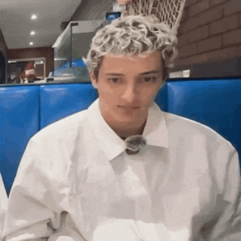 a young man with curly blonde hair is sitting in a blue chair in a restaurant .