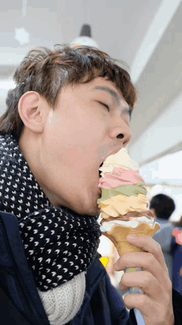 a man wearing a scarf is eating an ice cream cone with many different flavors