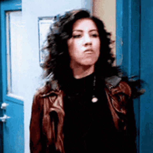 a woman in a leather jacket is standing in front of a blue door