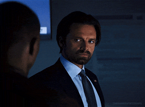 a man in a suit and tie is looking at another man in a dark room with the words thenameswintergifs below him