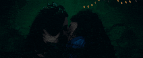 a woman with a crown is kissing another woman in a dark room