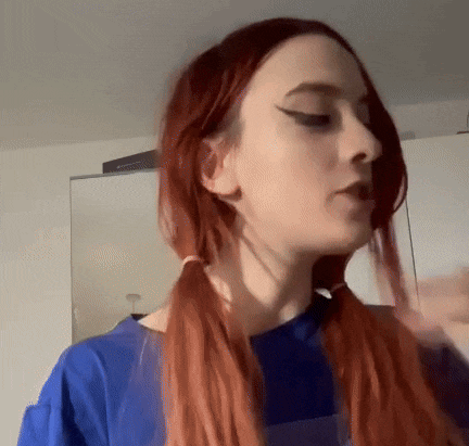 a woman with red hair and pigtails is wearing a blue shirt and looking at the camera .