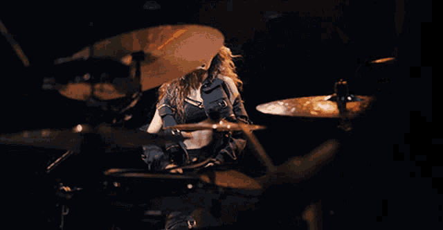 a woman in a denim jacket plays drums in a dark room