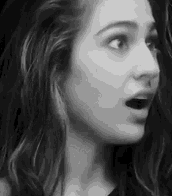 a black and white photo of a woman with her mouth open and a surprised look on her face .