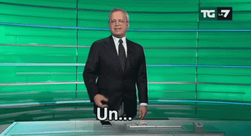a man in a suit and tie is standing in front of a green background and says un .