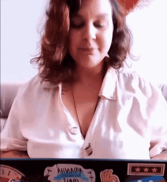 a woman in a white shirt is sitting in front of a laptop computer with stickers on it .