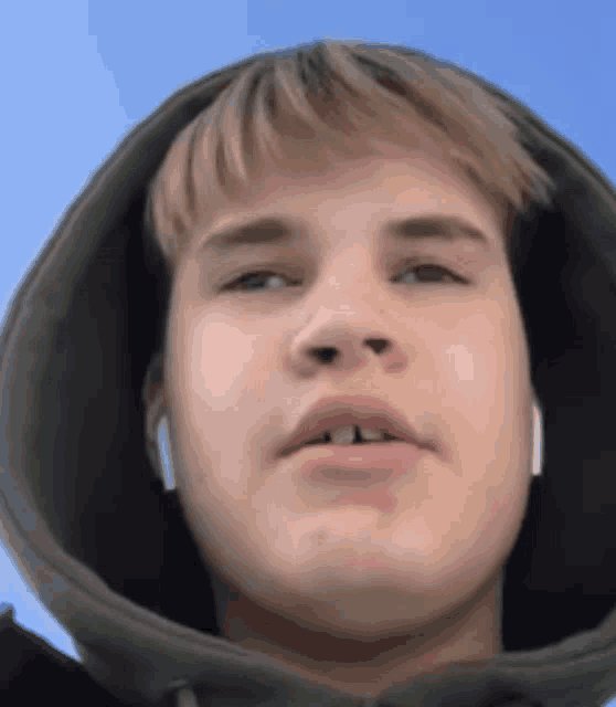 a young man wearing a hoodie and ear buds looks at the camera