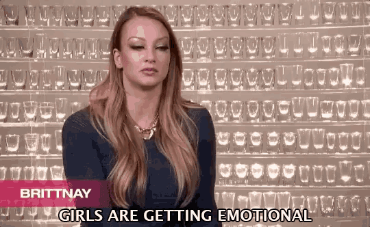 a woman is standing in front of a wall of shot glasses and says " girls are getting emotional "