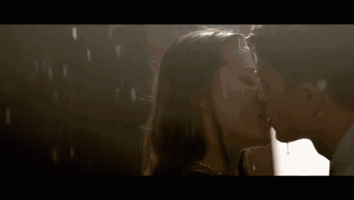 a man and a woman are kissing in the rain in a dark room .