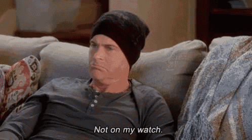 a man wearing a beanie is sitting on a couch and saying " not on my watch " .