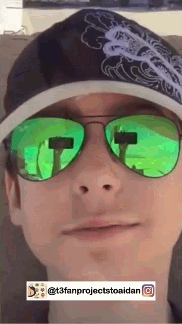 a person wearing green sunglasses and a black hat with the hashtag @t3fanprojecttoaidan