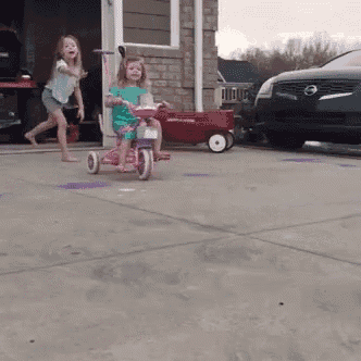 a little girl is riding a tricycle in a driveway next to a nissan truck