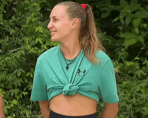 a woman wearing a green under armour t-shirt is standing in front of trees .