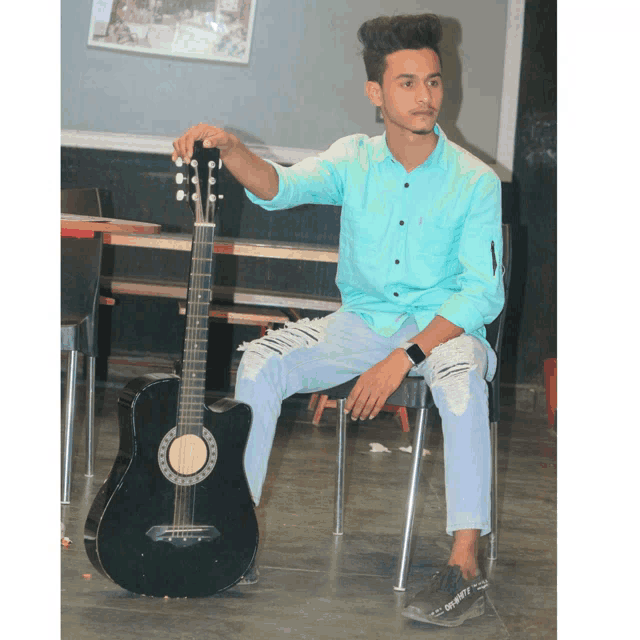 a young man is sitting on a chair holding a black guitar