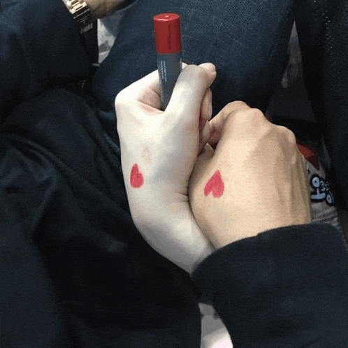 a person holding another person 's hand with a red heart on their wrist