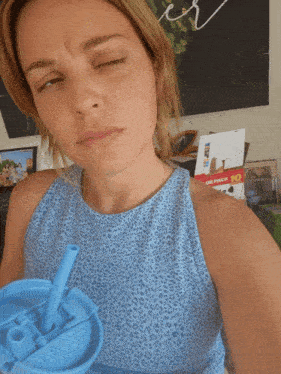 a woman in a blue tank top is holding a blue cup with a straw