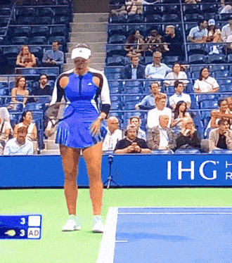 a woman in a blue skirt is standing on a tennis court in front of an ihg sign