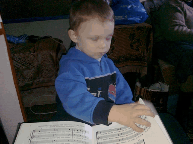 a young boy in a blue sweatshirt is reading a book of music