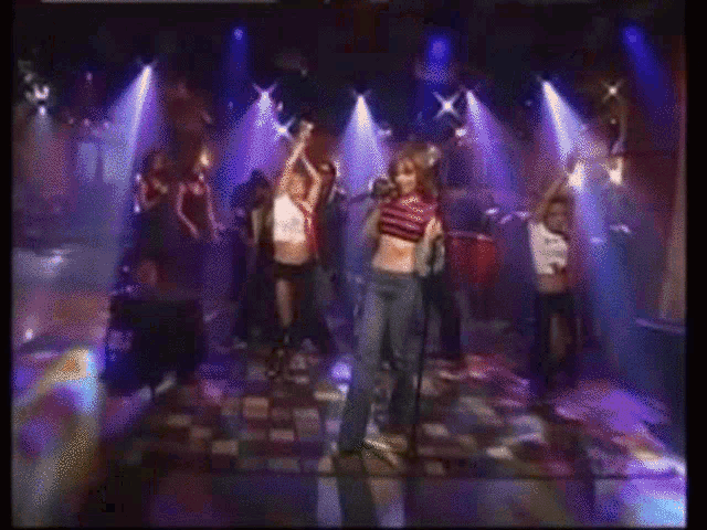 a woman in a striped shirt is dancing in a dark room with a man playing a guitar in the background