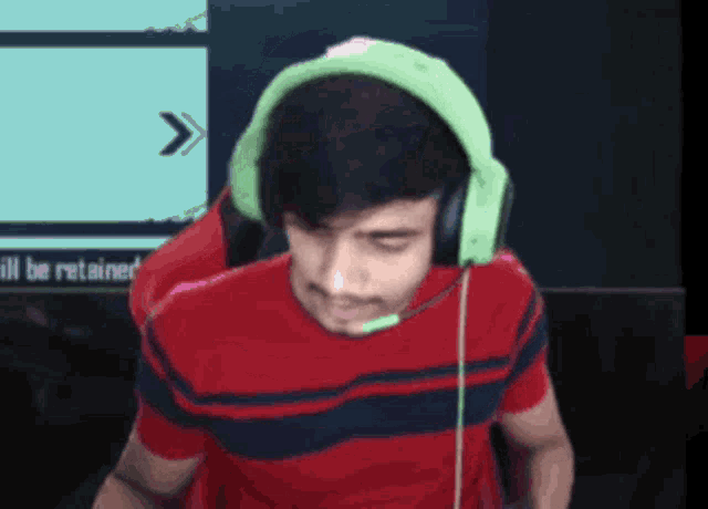 a man wearing green headphones and a red shirt is sitting in front of a screen that says will be retained