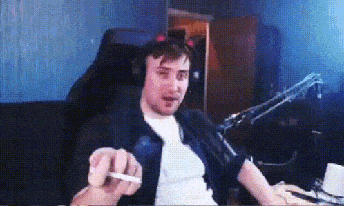 a man wearing headphones is smoking a cigarette while sitting in front of a microphone .