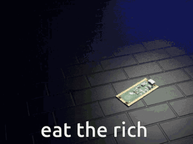 a computer chip is laying on a brick floor with the words " eat the rich " above it
