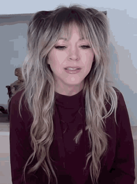a woman with long blonde hair is wearing a burgundy shirt