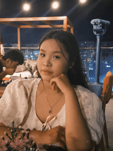a girl sitting at a table with her hand on her face