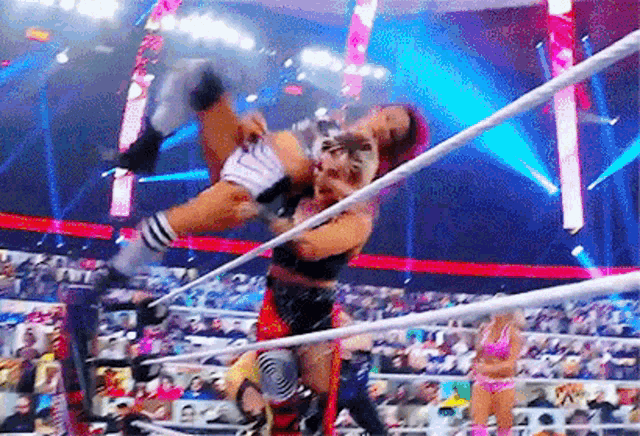 two women are wrestling in a ring while a crowd watches .