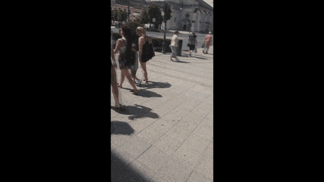 a group of women are walking down a sidewalk with a building in the background
