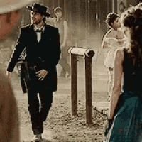 a man in a suit and hat is walking down a street next to a group of people .