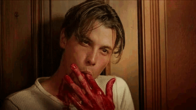 a man with blood on his hands is holding his mouth .