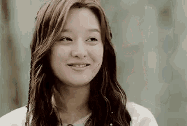a woman with long hair is smiling and wearing a white shirt .