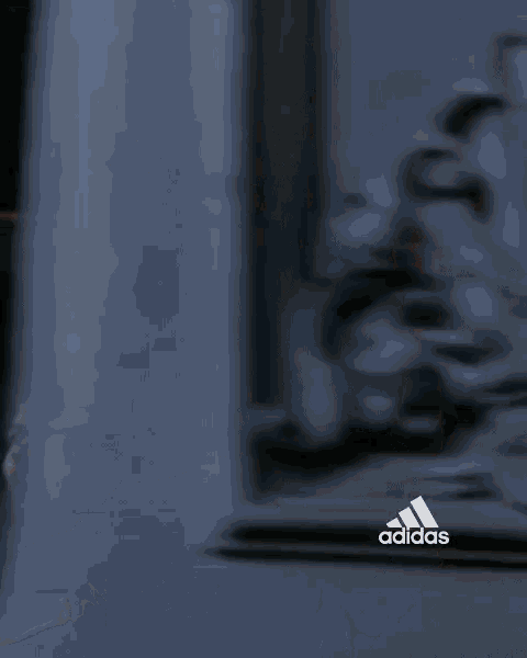 a man in a white adidas shirt is standing in front of a building