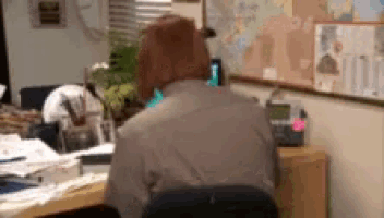 a woman sits at a desk in front of a bulletin board with a map on it