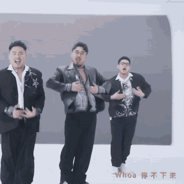 three men are dancing in front of a wall with whoa written on the bottom right
